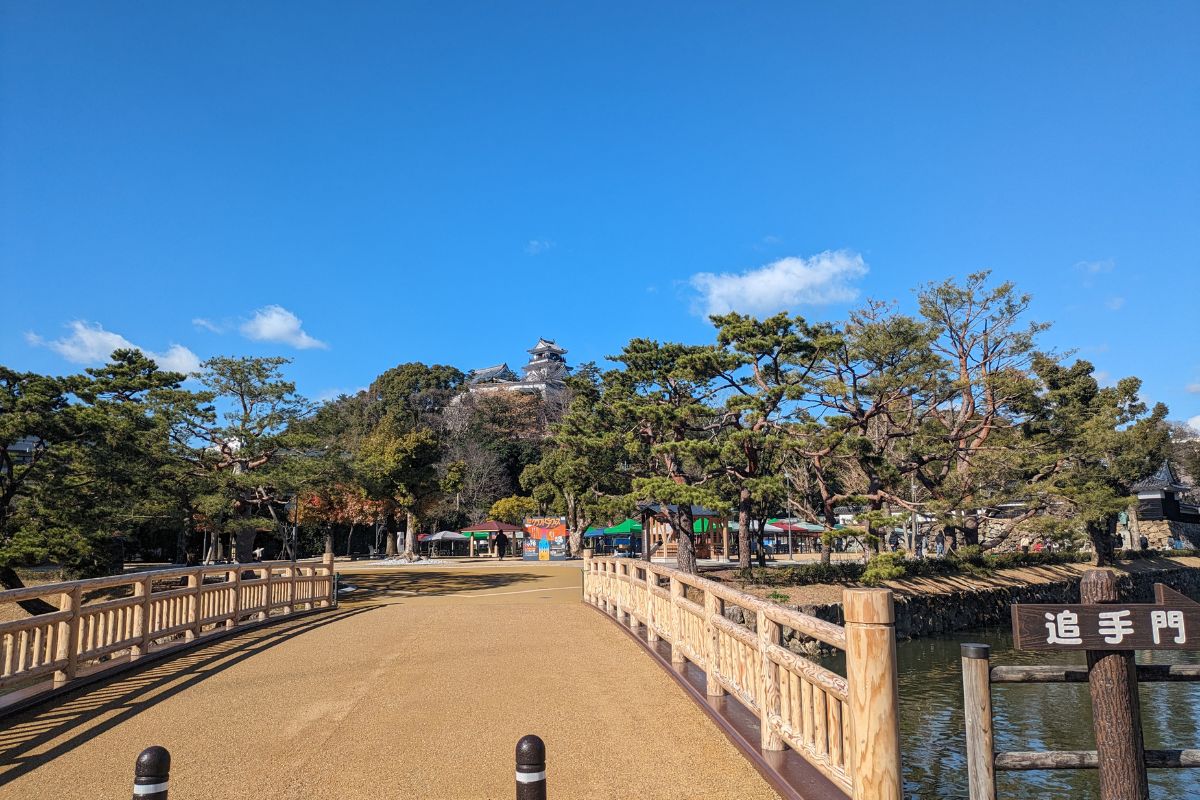 Entrance path and Otemon Gate leading to Kochi Castle on a sunny day, surrounded by pine trees and clear blue sky
