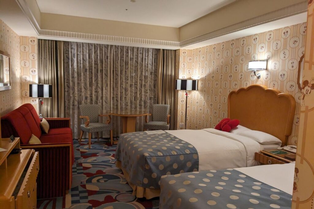  beautifully designed Disney Ambassador Hotel room featuring Mickey Mouse-themed wallpaper, cozy twin beds with polka dot bed runners, and elegant furniture, creating a magical Disney atmosphere.